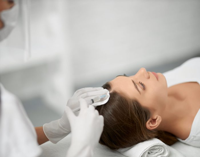 Side view of young cute brunette woman on procedure for improvements hair condition. Concept of different procedure for hair restoration in professional beauty salon.